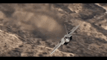 a fighter jet is flying in the air over a desert landscape .