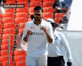 a man in a white shirt and sunglasses is standing in front of a row of red seats in a stadium .