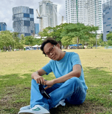 a man in a blue shirt sits on the grass in front of tall buildings