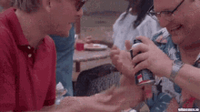 two men are sitting at a table and one of them is pointing at a coin that says ' i love you '