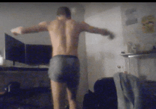 a shirtless man in boxer shorts stands in a dark room