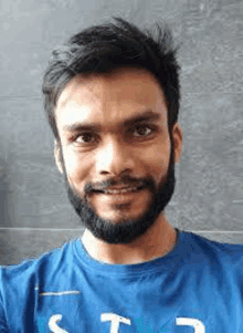 a man with a beard is wearing a blue t-shirt and smiling .