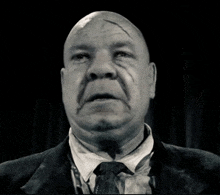 a bald man wearing a suit and tie has a scar on his forehead