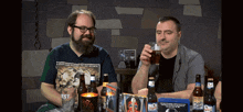 two men are sitting at a table with bottles of beer and one has a shirt that says best