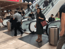 a woman stands on an escalator in front of an advertisement for samsung