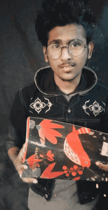 a young man wearing glasses is holding a book with a red fish on it that says ' sketchbook ' on the cover