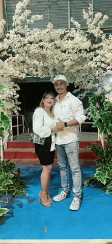 a man and woman are posing for a picture in front of a building with white flowers