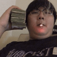 a man wearing glasses is smoking a cigarette and holding a stack of money in his hand