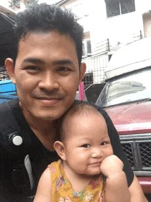 a man is holding a baby in front of a red truck