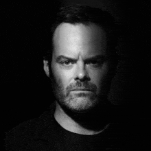 a black and white photo of a man with a beard and a black shirt .