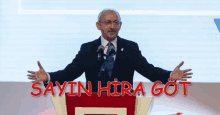 a man in a suit and tie stands at a podium with the words sayin hira got written above him