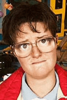 a young woman wearing glasses and a red jacket is making a funny face .