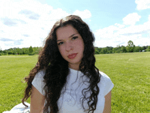 a woman with curly hair is sitting in a field