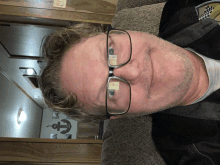 a man wearing glasses is sitting on a couch with an anchor on the wall behind him