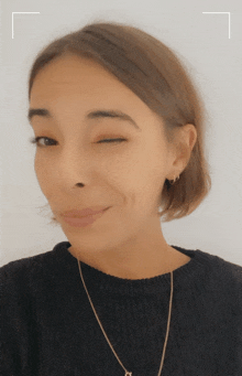 a woman wearing a black sweater and a gold chain winks at the camera