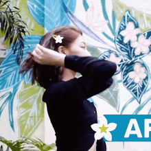 a woman with a flower in her hair is standing in front of a wall with flowers and leaves painted on it