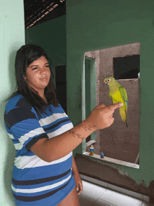 a woman in a blue and white striped shirt is holding a green parrot