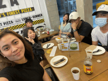 a group of people are sitting at a table in front of a sign that says ' finest pizza ' on it