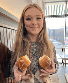 a woman is holding two buns with sesame seeds in her hands