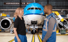 a man and a woman are standing in front of an airplane with a sign that says verboden te rol