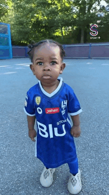 a little girl wearing a blue and white soccer jersey is standing on a street .