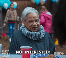 an older woman is sitting at a table with a plate of food and a red cup that says not interested