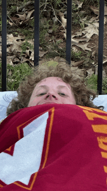 a man with curly hair is laying under a red and white blanket with a u on it