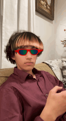 a young man wearing red sunglasses and a red shirt is sitting on a couch