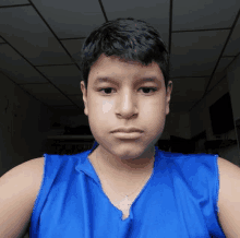 a young boy wearing a blue tank top and a necklace with a cross on it is taking a selfie .