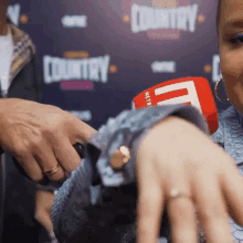 a close up of a woman 's hand with a microphone in front of a sign that says country .