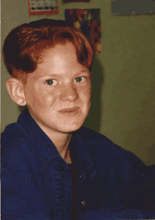 a young boy with red hair and freckles wears a blue jacket