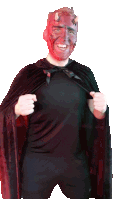 a man with red face paint and horns is wearing a black shirt and a black cape