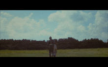 a man and a woman are walking through a field with trees in the background