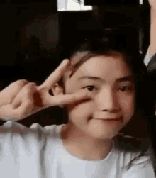 a young girl is making a peace sign with her fingers on her face .