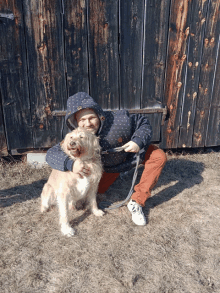 a man kneeling down with a dog on a leash in front of a wooden building