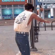 a man wearing a tank top that says ' customs ' on it is standing in front of a taxi sign