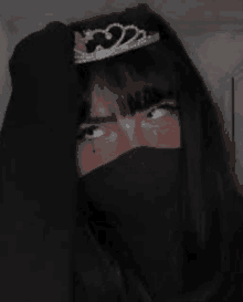 a girl wearing a black mask and a tiara on her head is looking at the camera .