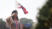 a woman salutes in front of a flag that says " philippines "