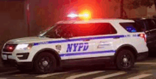 a white and blue nypd police car is driving down the street at night .