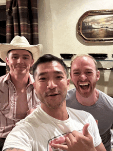 a man in a cowboy hat is laughing with two other men in front of a framed painting