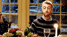 a man in a sweater is sitting at a table with a candle and a glass of wine .