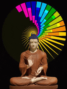 a statue of a buddha is sitting in front of a rainbow colored spiral .