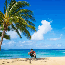 a man squatting on a sandy beach with a palm tree in the background