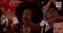 a woman with an afro is sitting at a table with other people at a golden globe awards event .