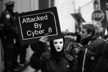 a person in a mask holds a sign that says attacked by cyber 8