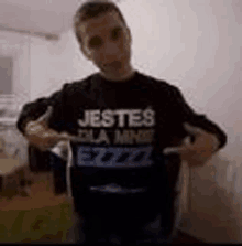 a man is standing in a room wearing a black t-shirt that says `` jestes dla mnie ezzzz '' .