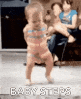 a baby is dancing on the floor while a woman holds a baby in her lap .