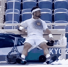 a man in a white shirt and white shorts is sitting on a tennis court holding a tennis racquet .