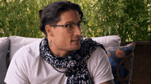 a man wearing glasses and a scarf has a tattoo on his left ear