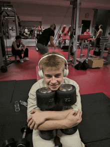 a man wearing headphones holds a pair of 22 pound dumbbells on his lap